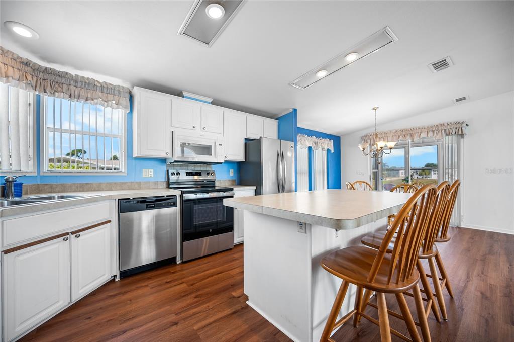 A kitchen with white cabinets, stainless steel appliances, a center island, and wood-look flooring — 9177 PINEHAVEN WAY, ENGLEWOOD, FL