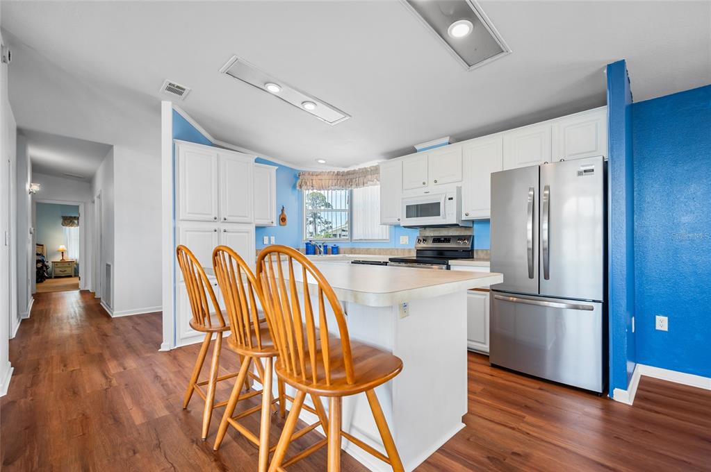 A kitchen with white cabinets, a central island with bar stools, and blue accent walls — 9177 PINEHAVEN WAY, ENGLEWOOD, FL
