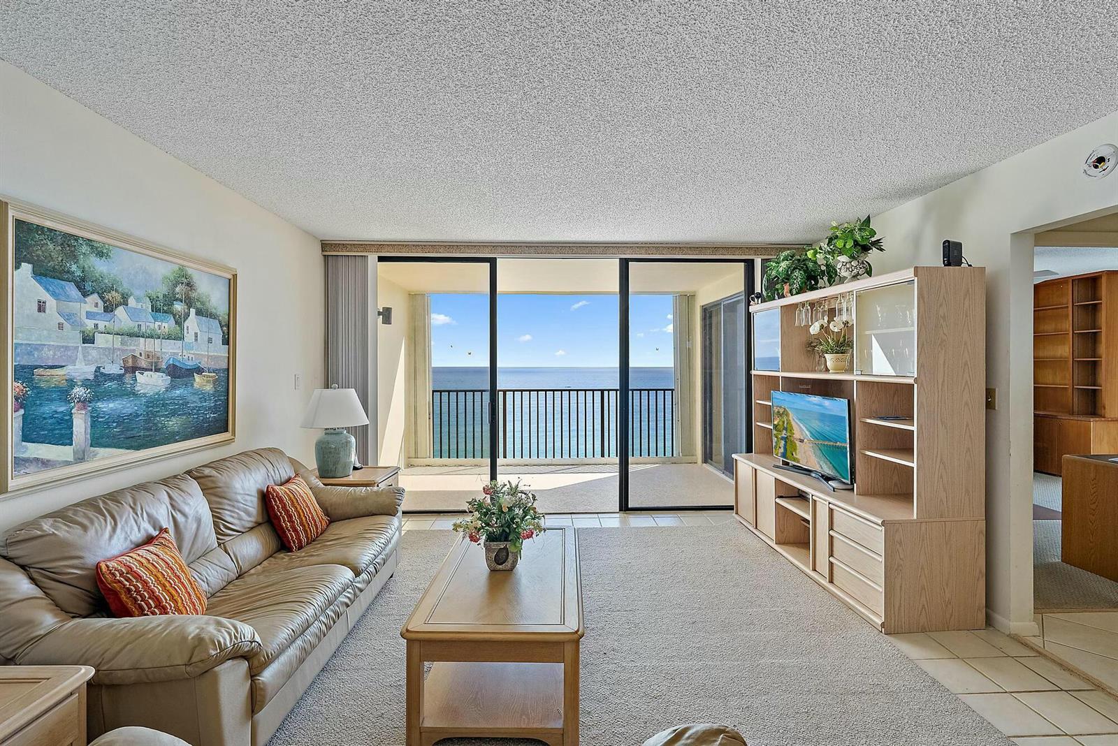 A living room with a leather sofa, entertainment center, and a balcony overlooking the ocean — 400 Ocean Trail Way # 1310, Jupiter FL 33477, JUPITER, FL