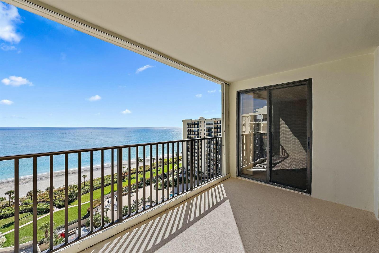 A balcony with a metal railing overlooks the ocean, beach, and a neighboring high-rise building — 400 Ocean Trail Way # 1310, Jupiter FL 33477, JUPITER, FL