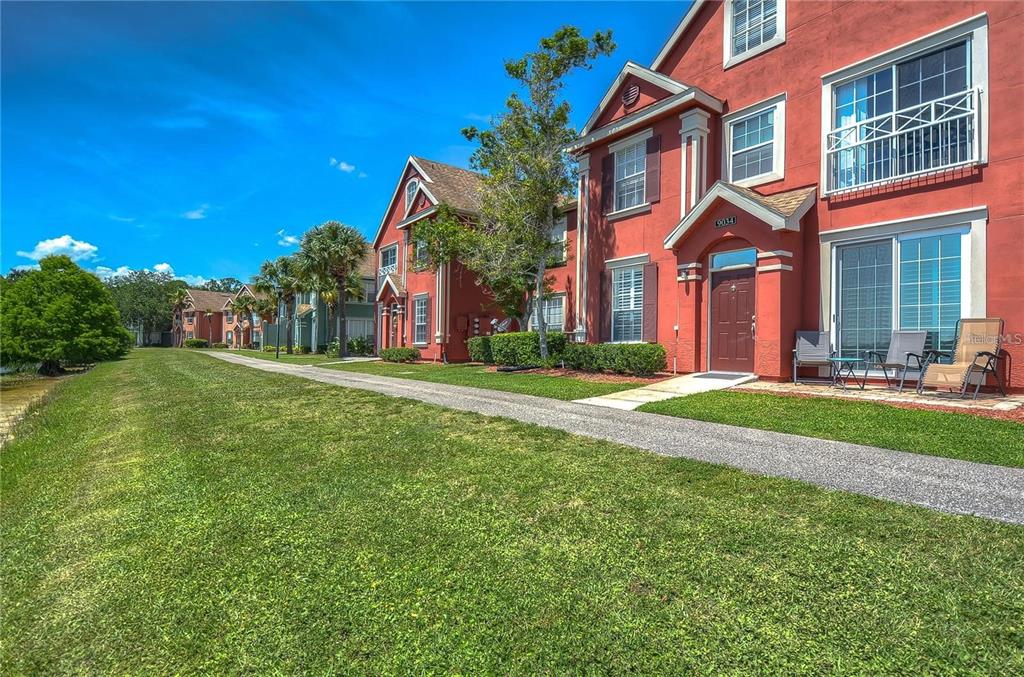 A multi-story red stucco apartment building features a paved walkway and a grassy lawn — 9034 LAKE CHASE ISLAND WAY UNIT 9034, TAMPA, FL