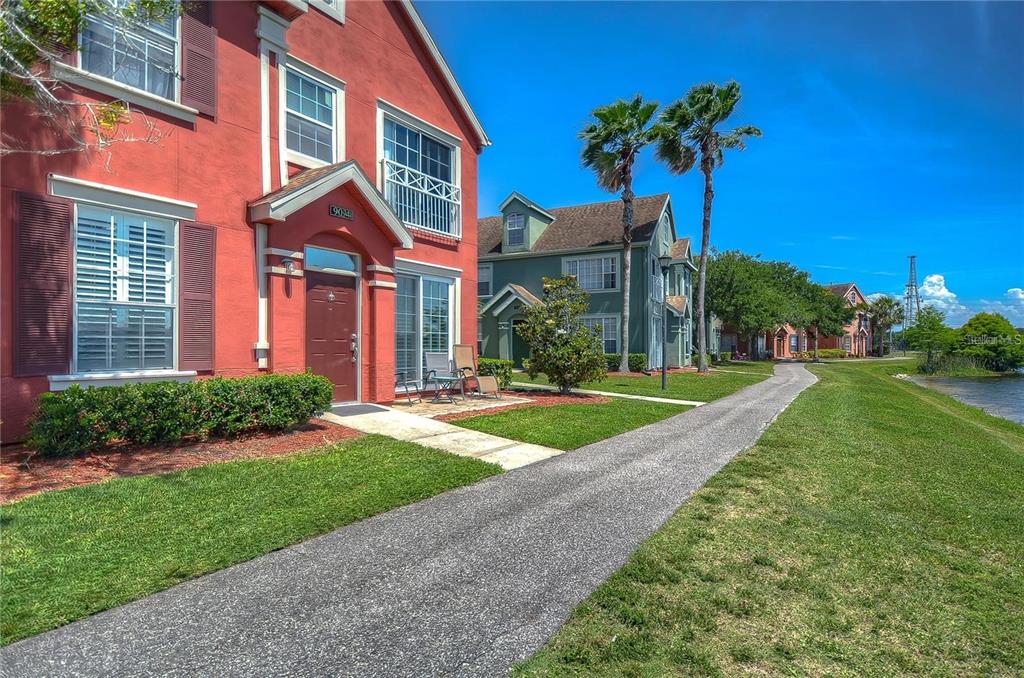A red two-story house with a paved walkway and palm trees beside a lake — 9034 LAKE CHASE ISLAND WAY UNIT 9034, TAMPA, FL