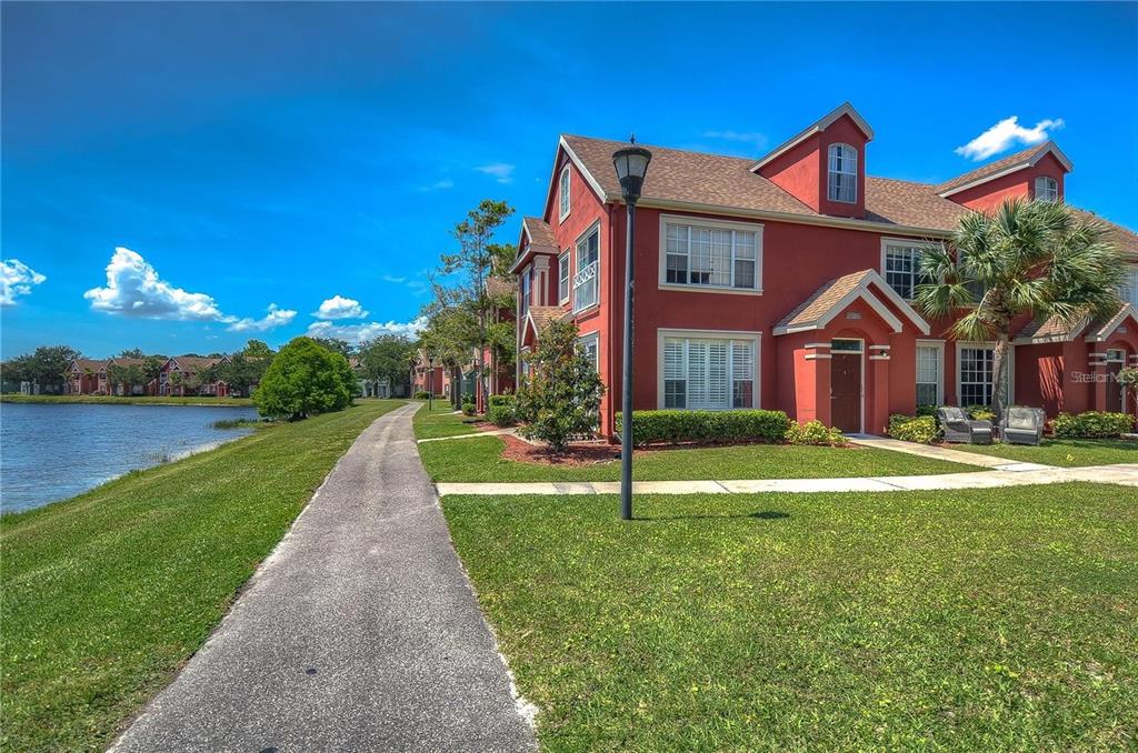 A red multi-story townhouse sits beside a paved walking path and a lake — 9034 LAKE CHASE ISLAND WAY UNIT 9034, TAMPA, FL