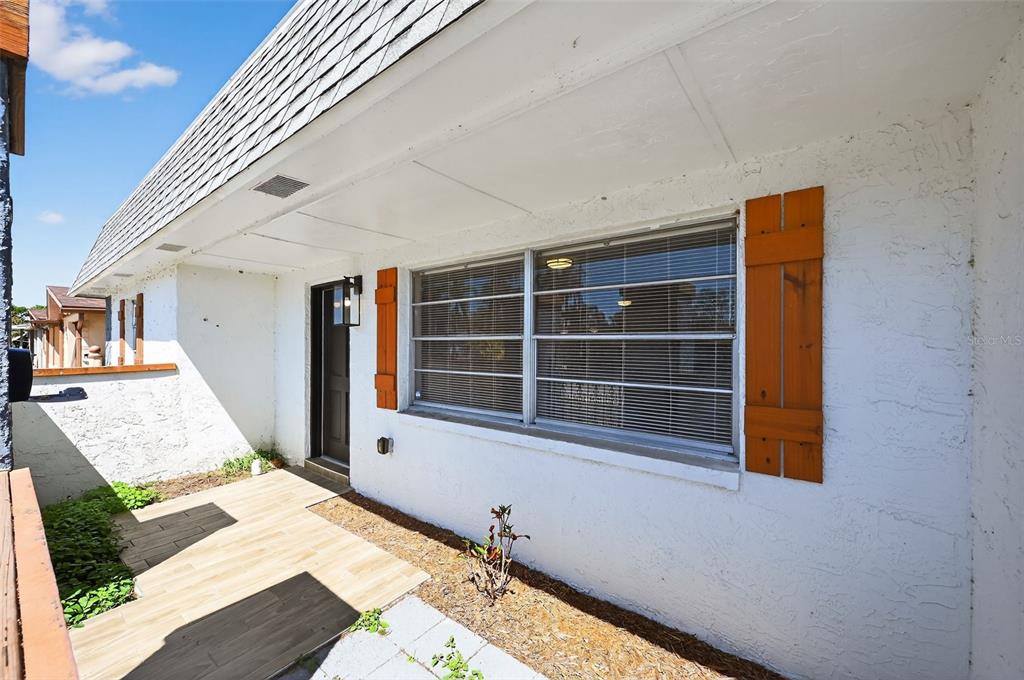 A white exterior wall features a large window with wooden shutters and a tiled patio — 7137 GULF HIGHLANDS DRIVE, PORT RICHEY, FL