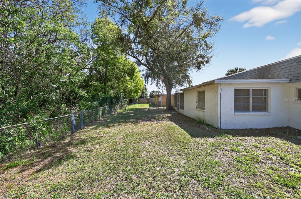 The side yard of a house features a chain-link fence and a large tree — 7137 GULF HIGHLANDS DRIVE, PORT RICHEY, FL