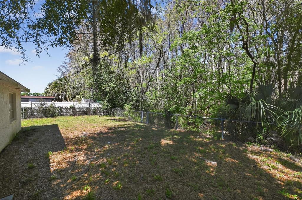 A grassy backyard features a chain-link fence bordering a dense wooded area — 7137 GULF HIGHLANDS DRIVE, PORT RICHEY, FL
