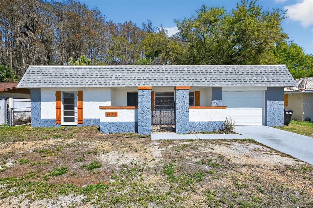 A single-story house with a white stucco facade, blue stone accents, and a gray roof — 7137 GULF HIGHLANDS DRIVE, PORT RICHEY, FL
