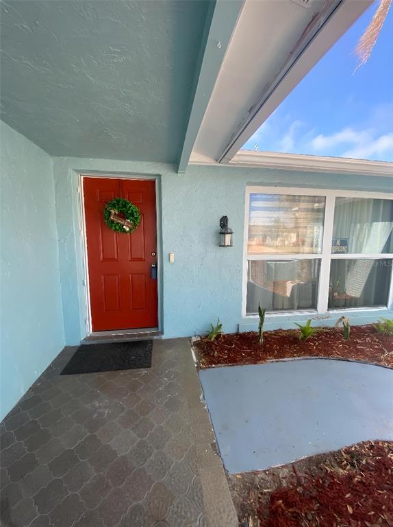 A light blue house exterior features a red front door with a wreath and windows — 1817 DARTMOUTH DRIVE, HOLIDAY, FL