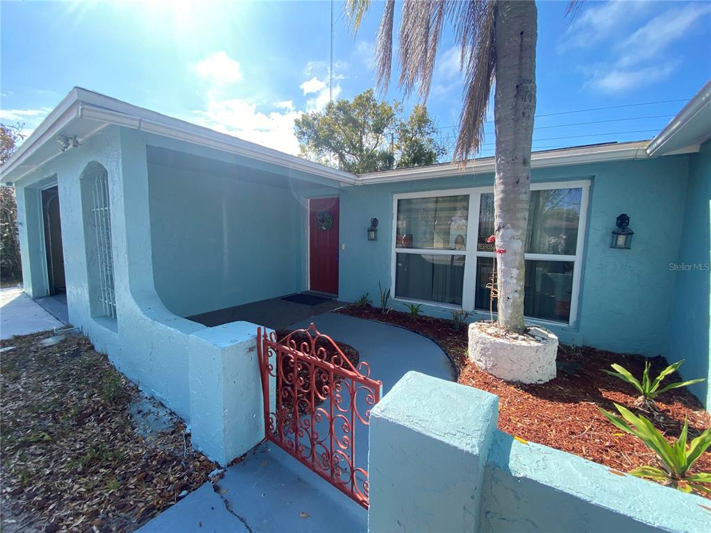 A light blue house exterior features a red front door and a decorative metal gate — 1817 DARTMOUTH DRIVE, HOLIDAY, FL