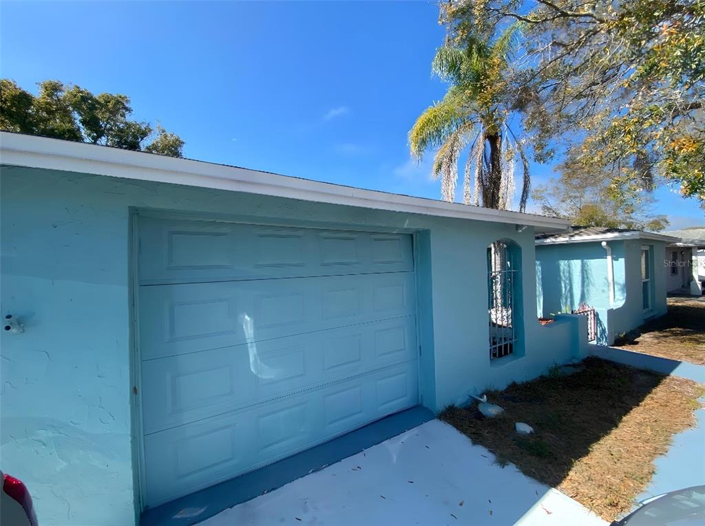 A light blue house exterior features a single-car garage and a small arched side window — 1817 DARTMOUTH DRIVE, HOLIDAY, FL