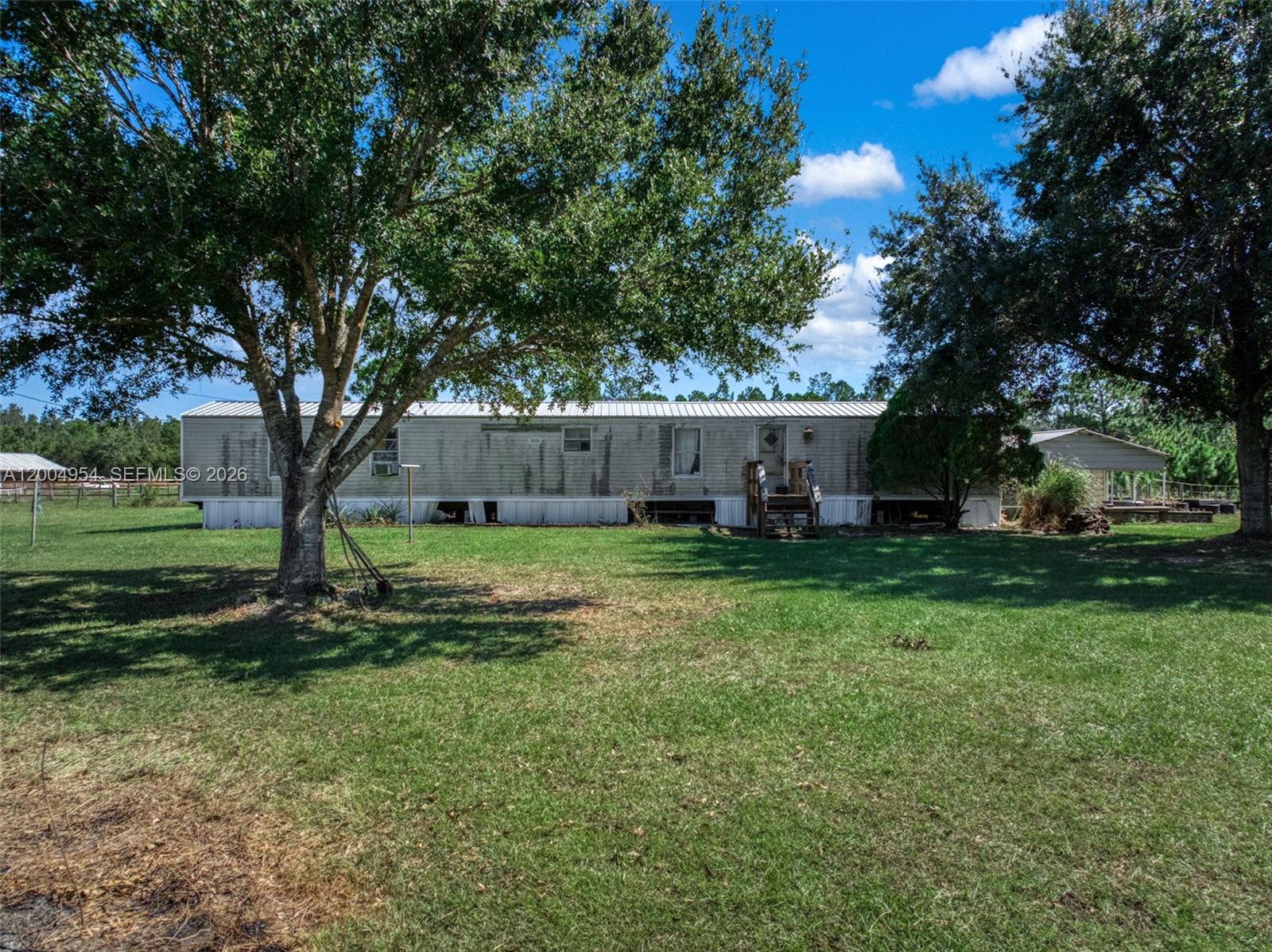 A single-story manufactured home sits on a grassy lot with large trees — 2316 Gem Stone, Sebring FL 33857, SEBRING, FL