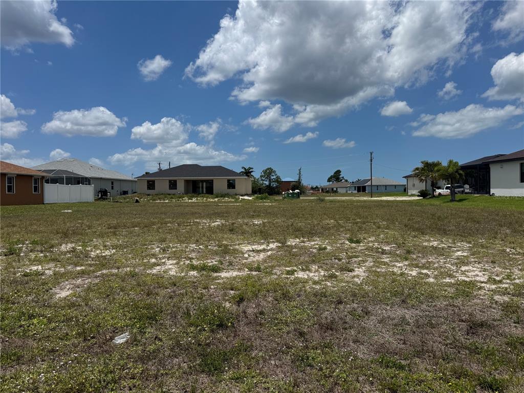 A vacant, grassy residential lot is surrounded by several single-family homes under a cloudy sky — 2018 NW 33RD AVENUE, CAPE CORAL, FL