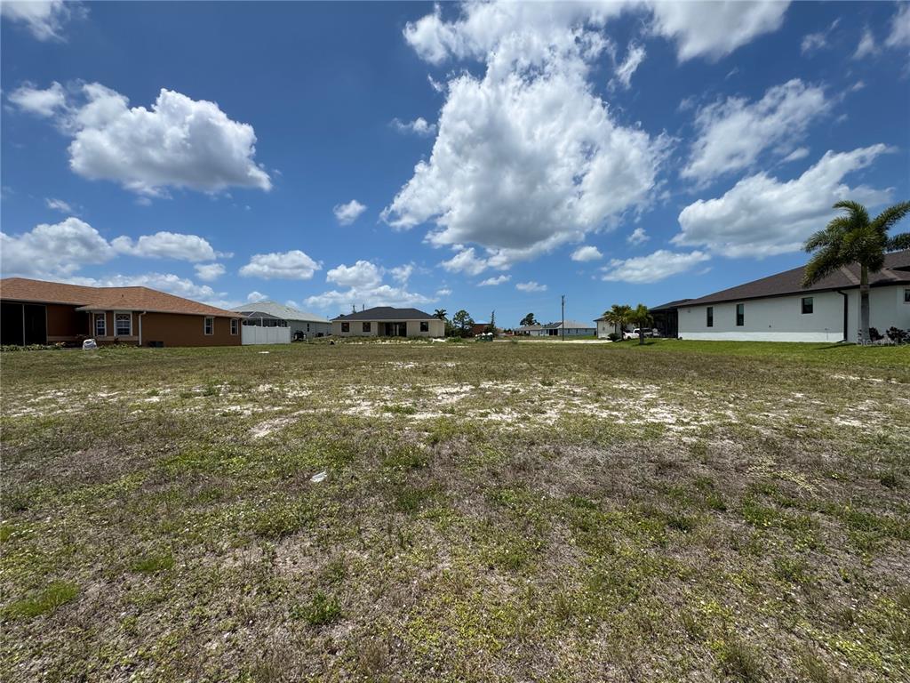 A vacant, grassy residential lot is surrounded by neighboring houses under a blue sky — 2018 NW 33RD AVENUE, CAPE CORAL, FL