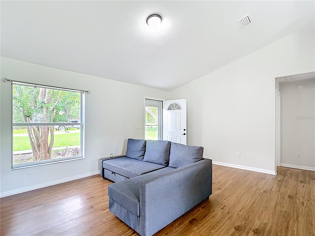 A living room with wood-look flooring, a gray sectional sofa, and a large window — 14939 SW 46TH CIRCLE, OCALA, FL