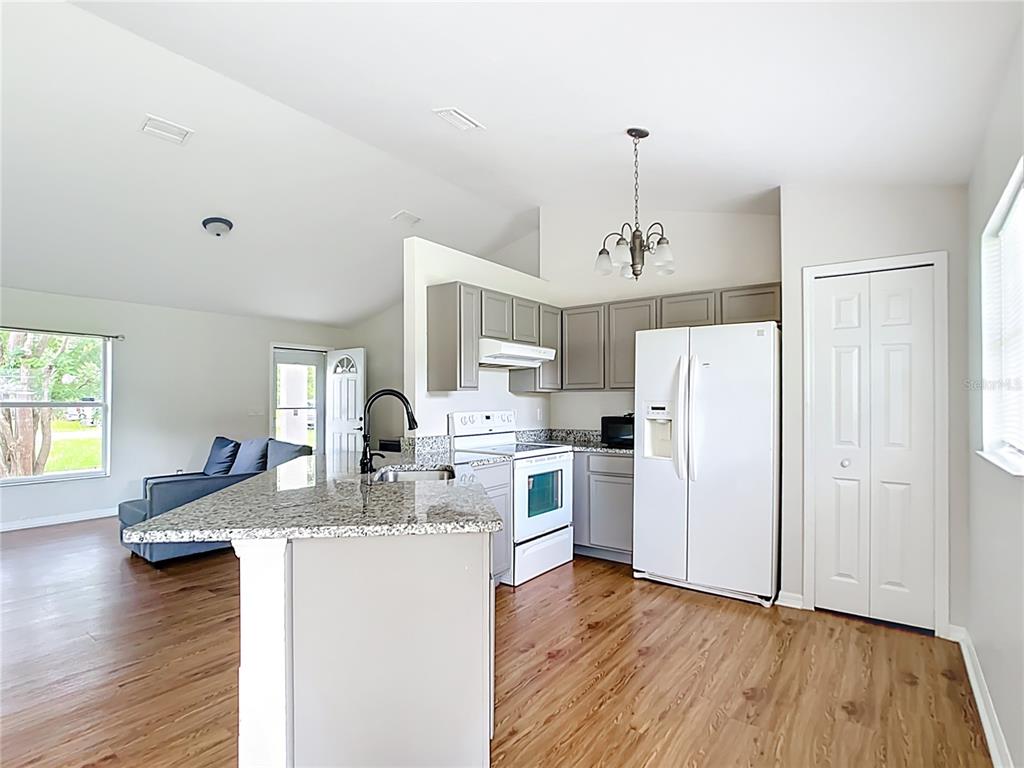 A kitchen with granite countertops, gray cabinets, and white appliances opens to a living area — 14939 SW 46TH CIRCLE, OCALA, FL