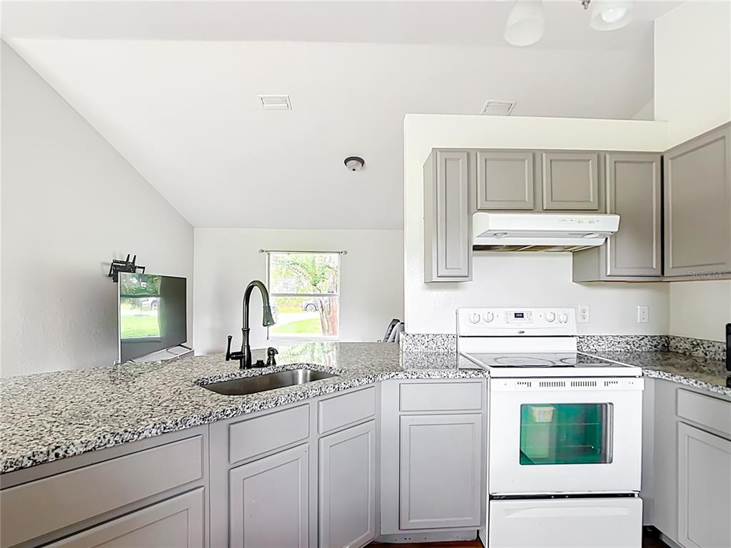 A kitchen features gray cabinets, granite countertops, a white stove, and a stainless steel sink — 14939 SW 46TH CIRCLE, OCALA, FL