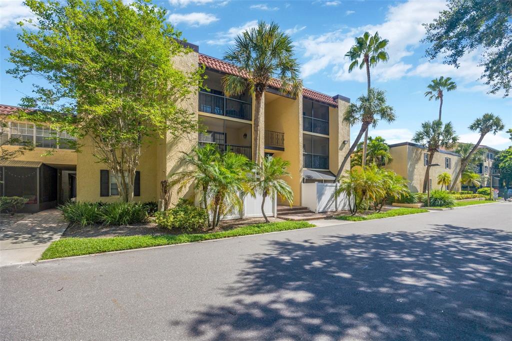 A three-story apartment building with yellow stucco walls, screened balconies, and surrounding palm trees — 5305 SAN SEBASTIAN COURT UNIT 127, TAMPA, FL