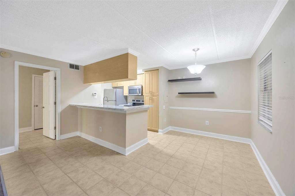A kitchen with a breakfast bar, light-colored cabinets, and tile flooring opens to a dining area — 5305 SAN SEBASTIAN COURT UNIT 127, TAMPA, FL