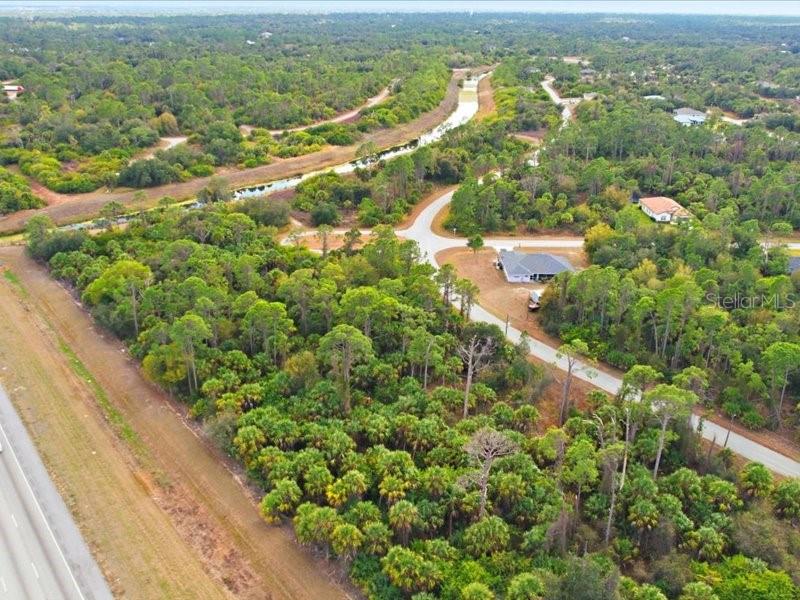 An aerial view shows a wooded lot adjacent to a road and a canal — 1126207439 BARCELONA DRIVE, NORTH PORT, FL
