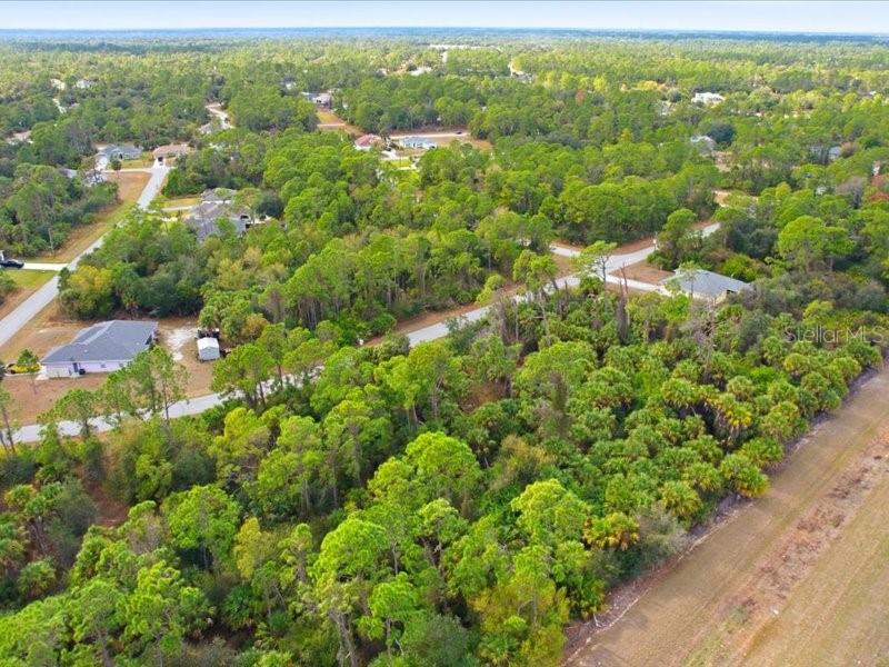 An aerial view shows a wooded residential lot surrounded by houses and paved roads — 1126207439 BARCELONA DRIVE, NORTH PORT, FL