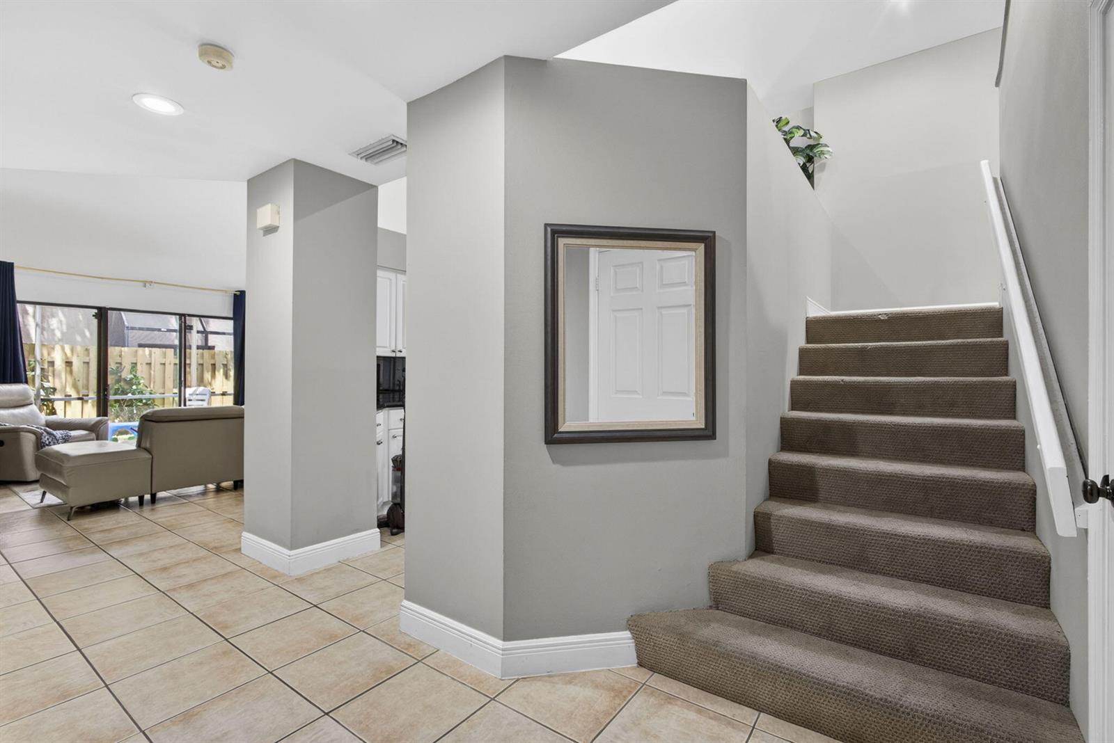A carpeted staircase sits beside a gray wall with a mirror and tiled flooring — 1726 Shoreside Circle, Wellington FL 33414, WELLINGTON, FL