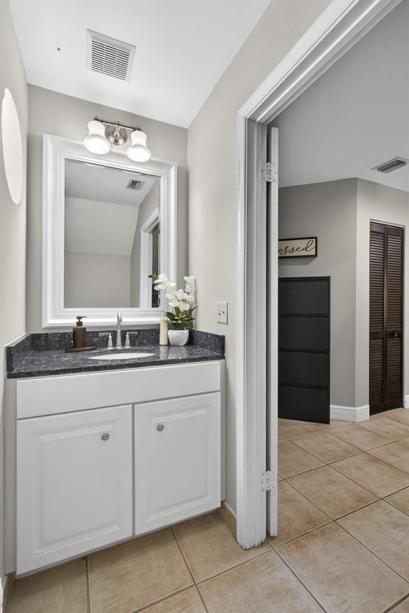 A bathroom vanity with a white cabinet, dark granite countertop, and a framed mirror — 1726 Shoreside Circle, Wellington FL 33414, WELLINGTON, FL