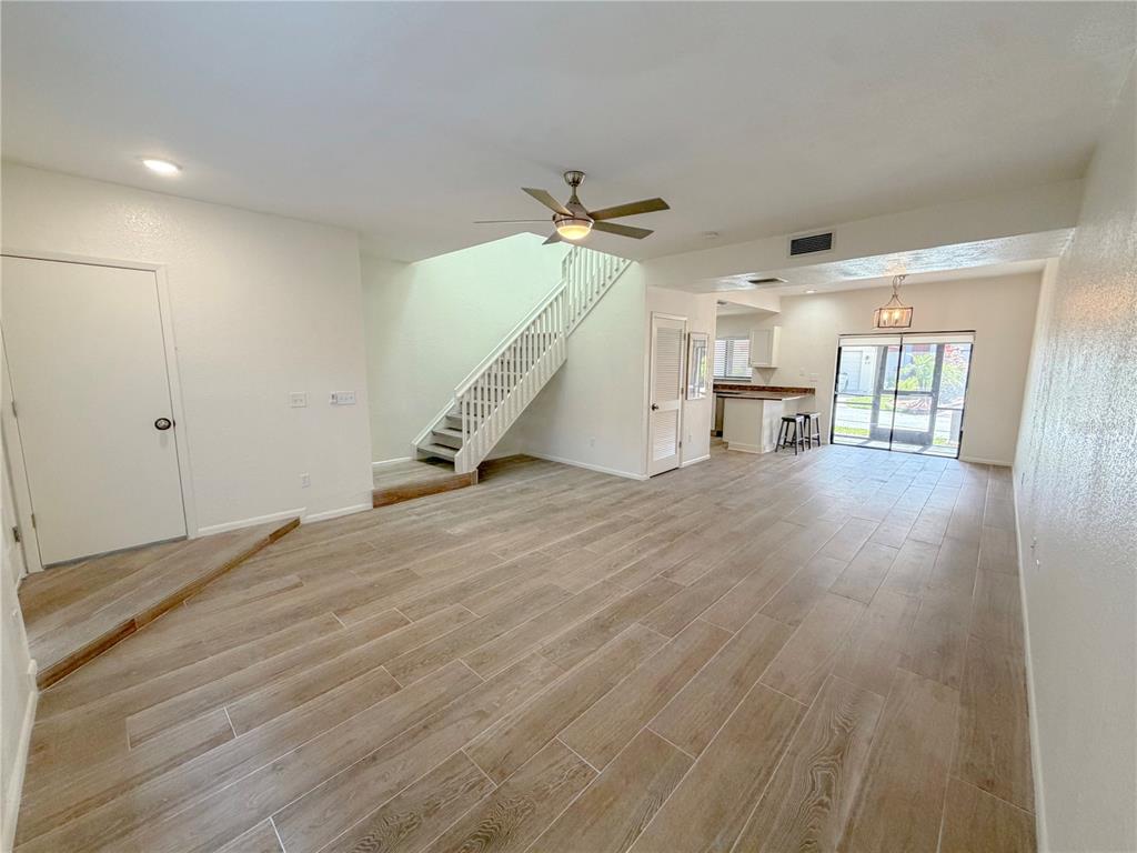 An open-concept living area features wood-look tile flooring, a staircase, and a kitchen beyond — 3460 COUNTRYSIDE BOULEVARD UNIT 60, CLEARWATER, FL