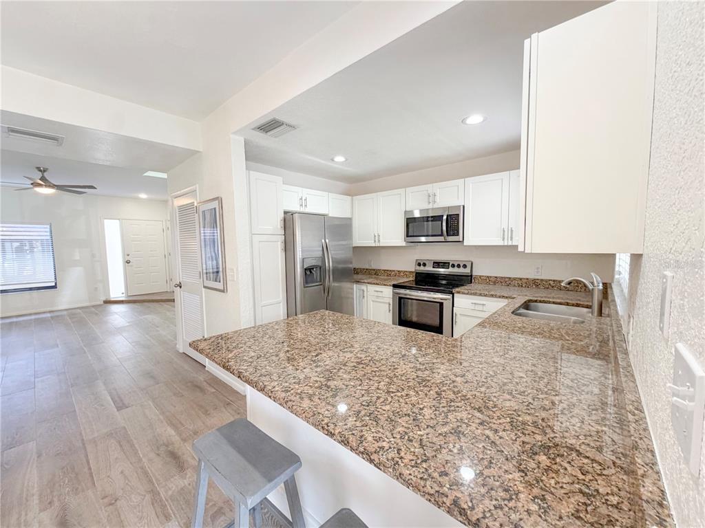 A kitchen features white cabinets, granite countertops, stainless steel appliances, and a breakfast bar — 3460 COUNTRYSIDE BOULEVARD UNIT 60, CLEARWATER, FL