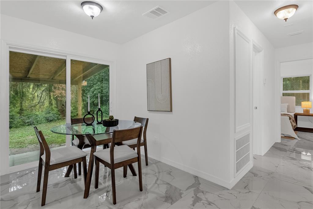A dining area with a glass table, four chairs, and sliding doors overlooking a wooded backyard — 107 FORD AVENUE, ALTAMONTE SPRINGS, FL