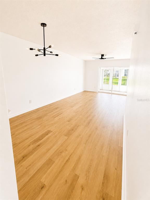 An empty room with light wood flooring, a modern chandelier, and sliding glass doors — 1420 OAK HILL DRIVE UNIT 102, DUNEDIN, FL