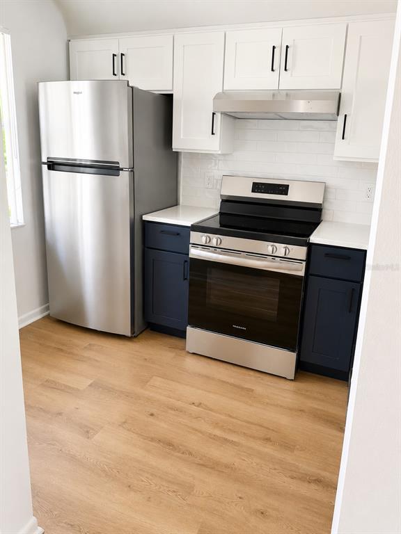 A kitchen features stainless steel appliances, white upper cabinets, and dark blue lower cabinets — 1420 OAK HILL DRIVE UNIT 102, DUNEDIN, FL