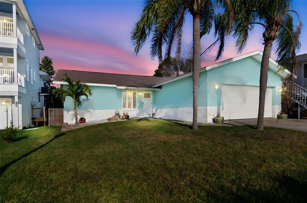 A light blue, single-story house with a two-car garage and palm trees at sunset — 216 176TH AVENUE E, REDINGTON SHORES, FL