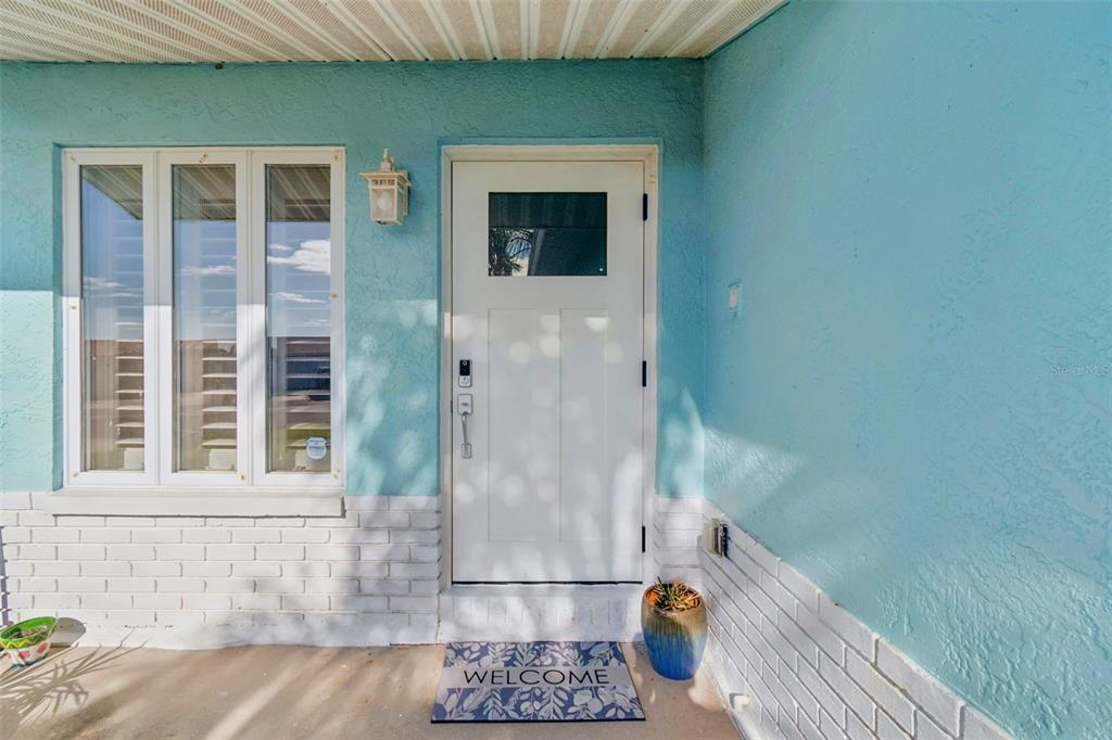 A white front door with a small window sits on a porch with light blue walls — 216 176TH AVENUE E, REDINGTON SHORES, FL