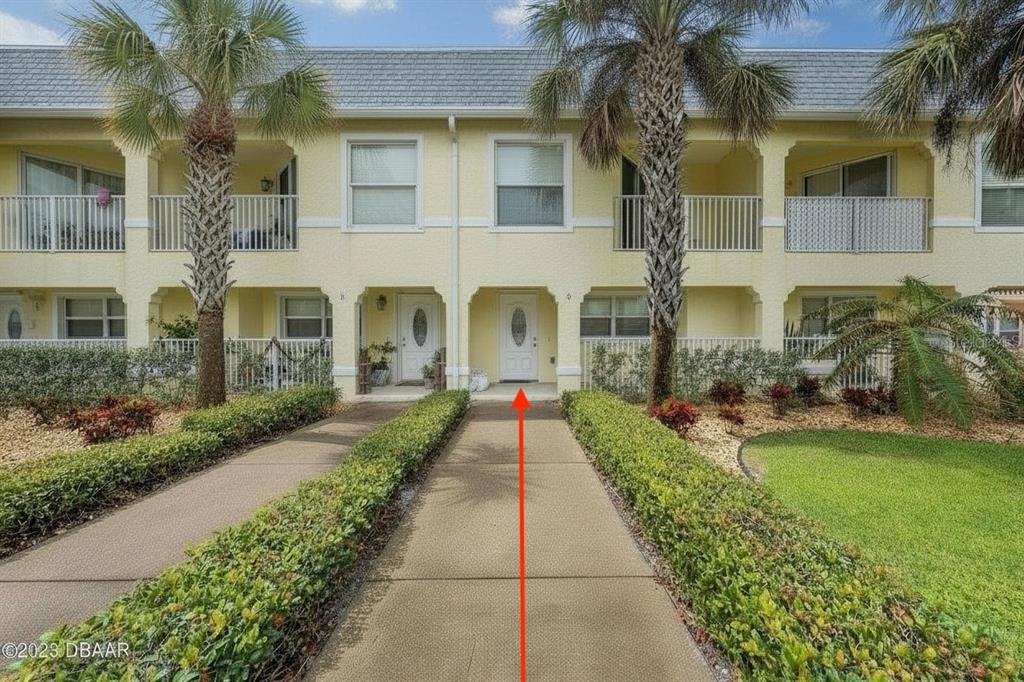 A two-story yellow townhouse exterior features a concrete walkway leading to a white front door — 3733 CARDINAL BOULEVARD UNIT 2, DAYTONA BEACH, FL