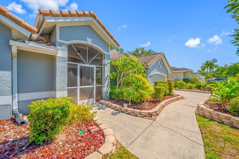 The exterior of a house features a screened entryway, a concrete walkway, and landscaped garden beds — 5321 GARDENS DR, SARASOTA, FL