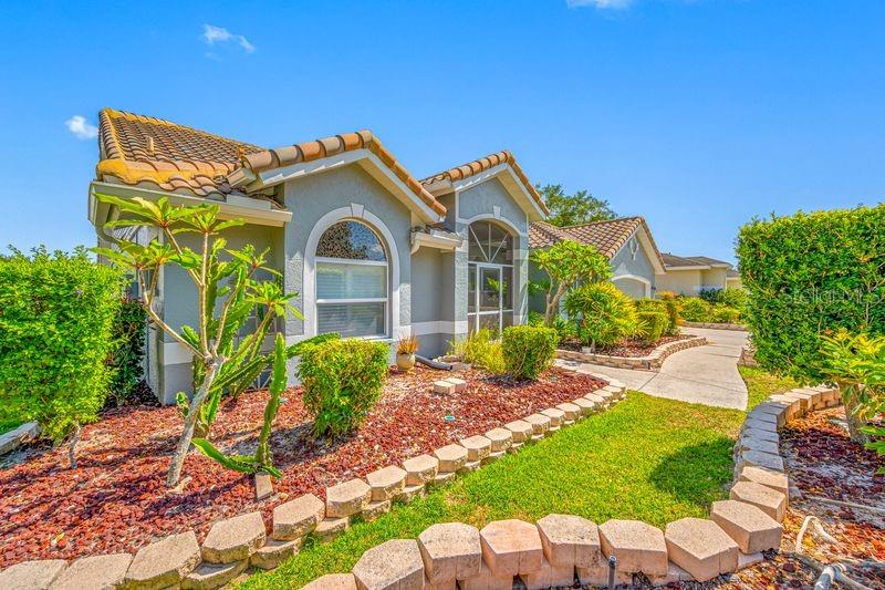 A single-story house with a tiled roof, gray stucco exterior, and a landscaped front yard — 5321 GARDENS DR, SARASOTA, FL