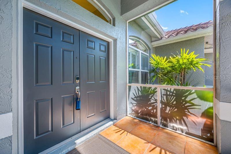 A dark gray double front door opens onto a tiled entryway with a screened-in porch — 5321 GARDENS DR, SARASOTA, FL