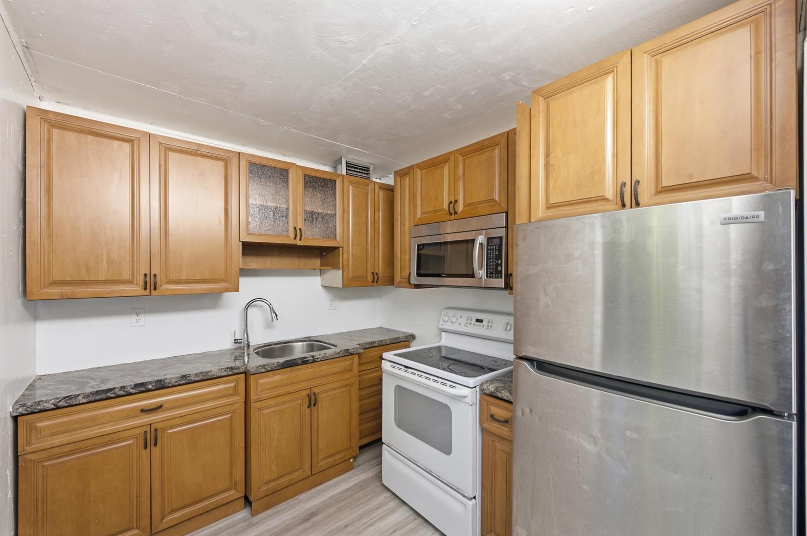 A kitchen features wood cabinets, stainless steel appliances, a white stove, and dark laminate countertops — 452 Normandy # J, Delray Beach FL 33484, DELRAY BEACH, FL