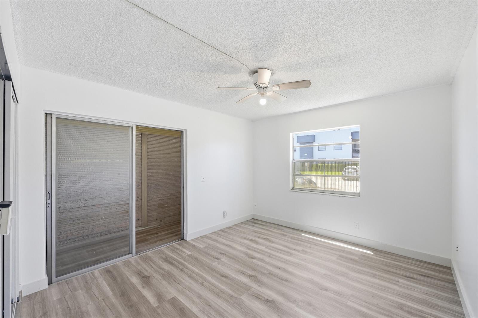 An empty room with white walls, wood-look flooring, a ceiling fan, and a sliding door — 452 Normandy # J, Delray Beach FL 33484, DELRAY BEACH, FL
