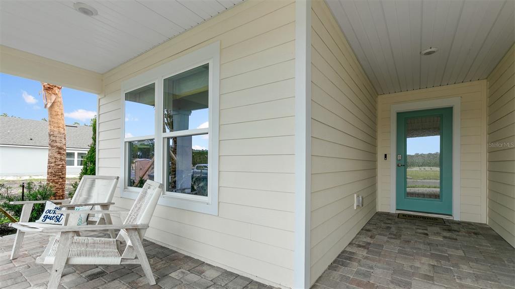 A covered front porch features light-colored horizontal siding, a teal front door, and two chairs — 58 HARDWOOD TRAIL, PALM COAST, FL