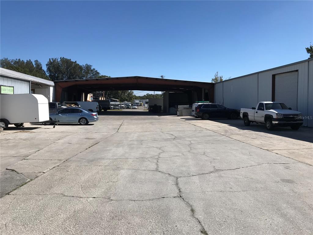 A paved outdoor lot sits between two industrial warehouse buildings under a clear blue sky — 5010 N COOLIDGE AVENUE, TAMPA, FL