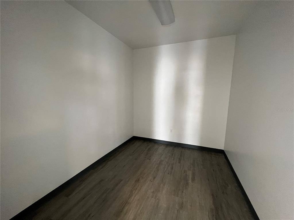 A small, empty room features white walls, dark wood-look flooring, and a ceiling light fixture — 5010 N COOLIDGE AVENUE, TAMPA, FL
