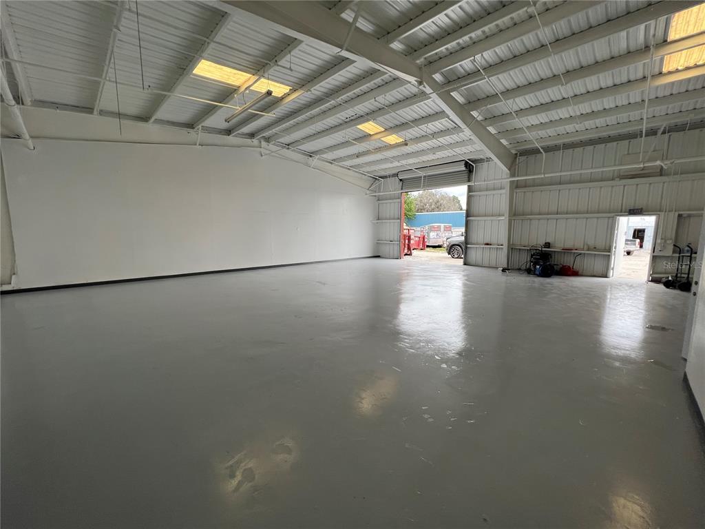 An empty warehouse interior features a gray concrete floor, white walls, and a roll-up door — 5010 N COOLIDGE AVENUE, TAMPA, FL