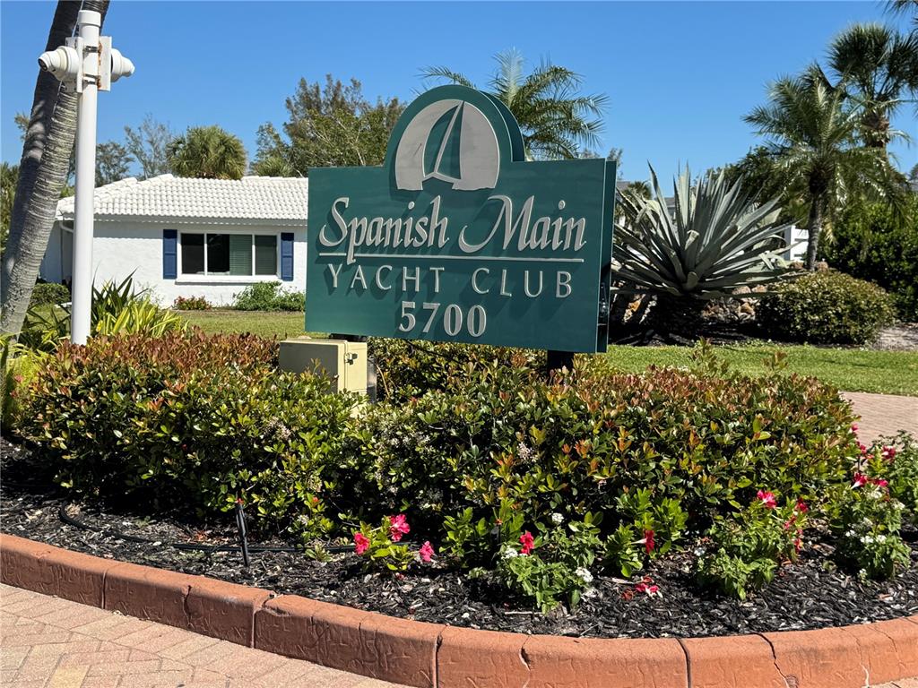 A green sign for Spanish Main Yacht Club stands in a landscaped garden bed — 718 SPANISH DRIVE N, LONGBOAT KEY, FL