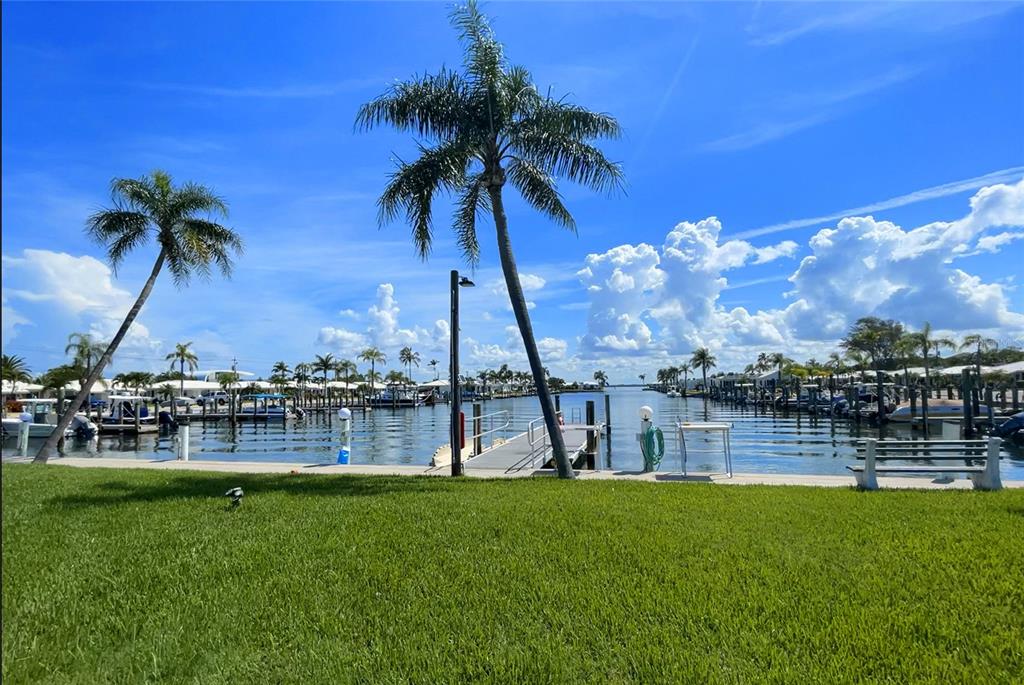 A grassy lawn overlooks a boat canal lined with docks and palm trees under blue skies — 718 SPANISH DRIVE N, LONGBOAT KEY, FL