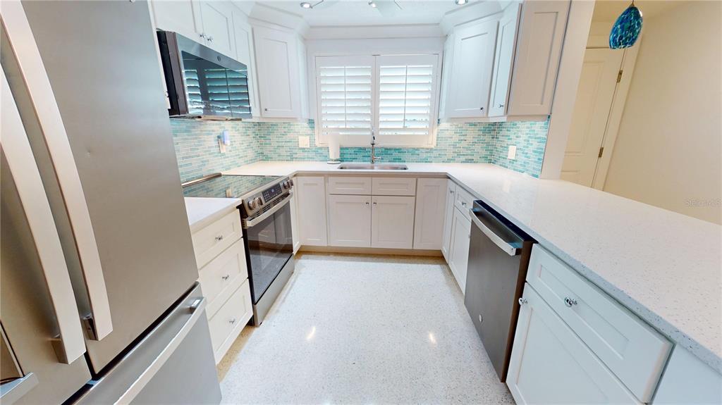 A kitchen features white cabinetry, stainless steel appliances, a light countertop, and blue tile backsplash — 718 SPANISH DRIVE N, LONGBOAT KEY, FL