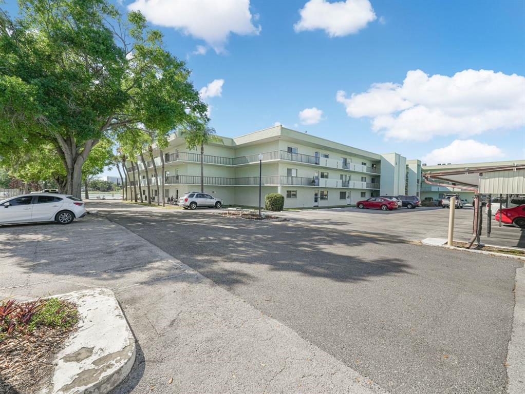 A three-story apartment building with a parking lot and mature trees in the foreground — 1130 N LAKE PARKER AVENUE UNIT A201, LAKELAND, FL