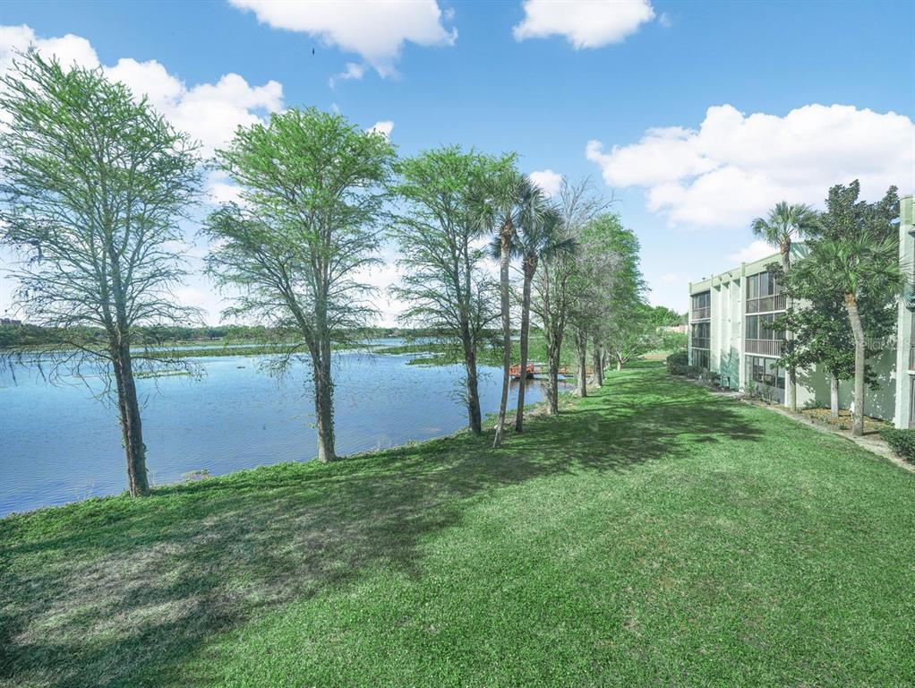 A grassy lawn leads to a lake lined with trees beside a multi-story apartment building — 1130 N LAKE PARKER AVENUE UNIT A201, LAKELAND, FL