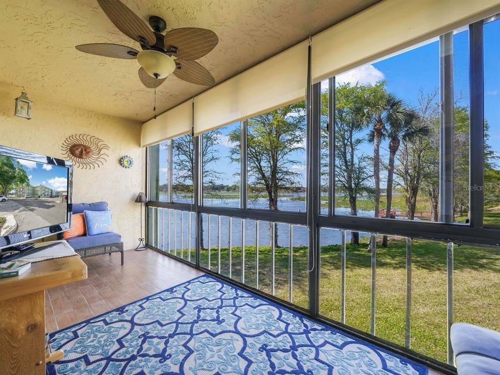 A screened-in porch with a ceiling fan, patterned rug, and large windows overlooking a lake — 1130 N LAKE PARKER AVENUE UNIT A201, LAKELAND, FL