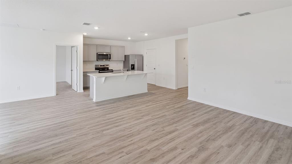 An open-concept kitchen with a white island and gray cabinets overlooks a living area — 7876 FORREST FOX WAY, LAKELAND, FL
